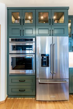 a stainless steel refrigerator and oven in a kitchen with green cabinets, wood flooring and hardwood floors