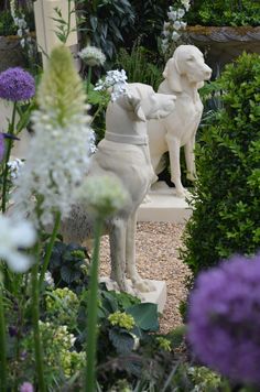 a statue of a dog and a white dog in a garden with purple and white flowers