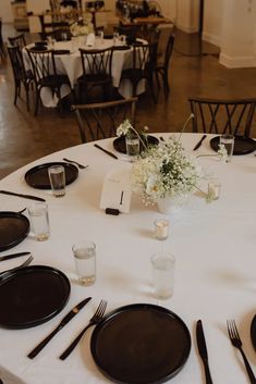 the table is set with black and white plates, silverware, and flower centerpieces