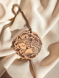 Snuggle Up with Nature: Adorable Sleeping Fox Design Embrace the serenity of nature with this beautifully crafted wood necklace, featuring a peacefully sleeping fox nestled amongst delicate foliage. Expertly engraved in a whimsical, hand-drawn style, this pendant is perfect for nature enthusiasts and those who adore woodland charm. Unique & Whimsical Design: The peaceful fox, surrounded by intricate leaves and natural elements, creates a scene full of woodland magic. Ideal for adding a touch of charm to your daily look. Hand-Engraved Craftsmanship: Every detail, from the fox's fur to the fine leaves, is meticulously engraved to bring out the pendant's intricate artistry. One-of-a-Kind Piece: Due to the handmade nature of this product, each necklace may have slight variations in the wood gr Fox Necklace, Foxes Necklace, Woodland Fox, Fox Design, Whimsical Design, Wood Necklace, Wood Pendant, Natural Elements, Gifts For Nature Lovers