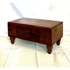 a wooden box with writing on it sitting on top of a white cloth covered floor