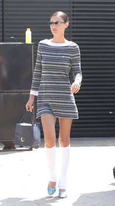 a woman walking down the street with her hand in her pocket and wearing knee high socks