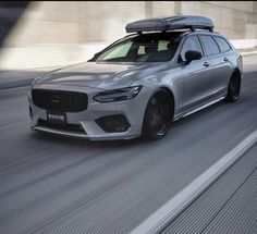 a silver car driving down the road with a surfboard on top