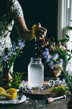 a person is pouring water into a jar with lemons and lavender flowers in the background