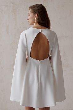 the back of a woman wearing a white dress with an open back and long sleeves