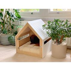 a dog house made out of cardboard with a cat in it's bed next to a potted plant