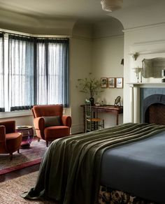 a bedroom with a bed, chair and fireplace in the corner next to two windows