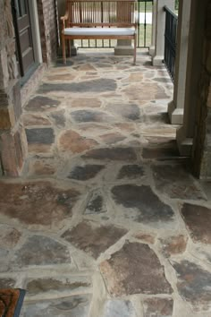 a stone walkway with a bench in the background and an open door leading to another room