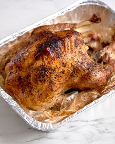 a roasting chicken in a foil container on a marble counter top with the lid off