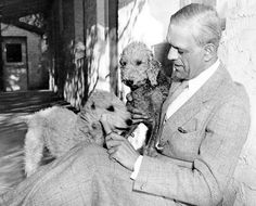 a man holding two poodles in his lap while sitting on the ground next to a building