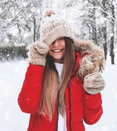 a woman wearing a red jacket and hat in the snow with her hands on her head