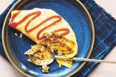 a blue plate topped with an omelet covered in ketchup and rice