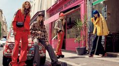 three women sitting on the back of a car in front of a pink storefront