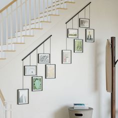 a white staircase with pictures on the wall and a trash can under it next to a stair case