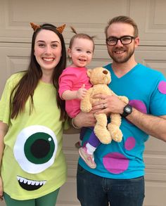 a man and woman holding a baby in front of a garage door with a monster costume on