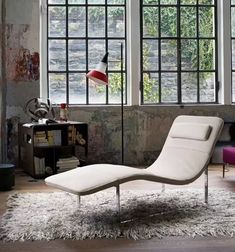 a white chaise lounge chair sitting on top of a rug in front of two windows