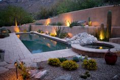 an outdoor pool surrounded by rocks and cactus plants with lights in the background at night