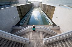 a woman standing at the top of some stairs looking down on her reflection in the water