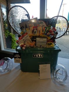 a green basket filled with assorted items on top of a white cloth covered table