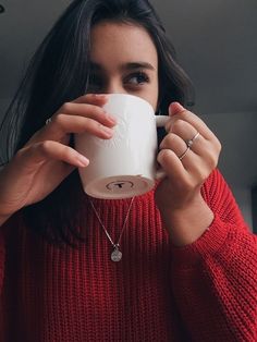 a woman in a red sweater is drinking from a white coffee cup with her hands