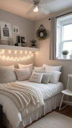 a white bed sitting under a window next to a light filled wall with pictures on it