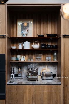 a kitchen with wooden cabinets and shelves filled with coffee pots, cups, and other items