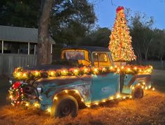 an old truck is decorated with christmas lights and a tree in the back yard at night