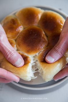 two hands reaching for a bun on a plate