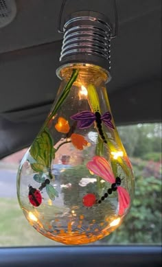 a light bulb hanging from the side of a car with flowers and bugs on it