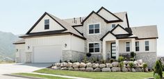 a large house with two garages and landscaping on the front lawn, surrounded by mountains