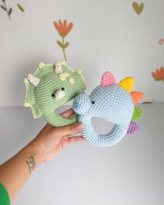 two crocheted stuffed animals are being held up by someone's hand in front of a floral wallpaper