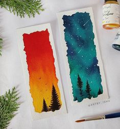 two watercolor cards with trees on them next to some paintbrushes and glue