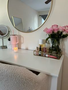 a white vanity with pink roses and candles on the counter in front of a round mirror