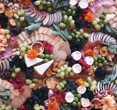 an assortment of cheeses, fruits and meats arranged on a platter with leaves