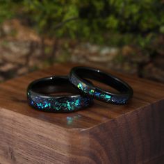 two black rings with blue and green opal inlays on top of a wooden box