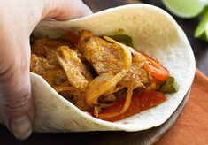 a person is holding a tortilla filled with chicken and peppers