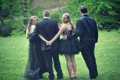 three people in formal wear are holding hands and standing on the grass with trees in the background