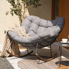 a grey rocking chair sitting on top of a rug next to a table with a cup