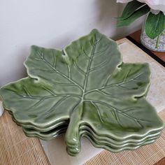 a green leaf shaped dish sitting on top of a table next to a vase with flowers