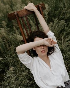 a woman is sitting in the grass with her arm over her head while holding onto a chair