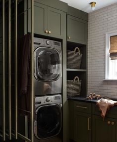 a washer and dryer in a small room with green cabinetry, brown flooring and white brick walls