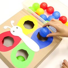 a child's hand is playing with colorful plastic balls in front of a cardboard box