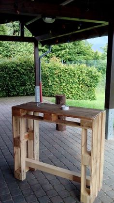 a wooden table sitting on top of a brick floor next to a lush green field