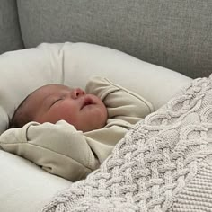 a baby wrapped in a blanket is laying on a couch with its eyes closed and it's head resting on the pillow