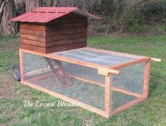 a chicken coop in the middle of a grassy area with trees and bushes behind it