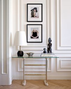 a glass table with two pictures on the wall behind it and a lamp next to it