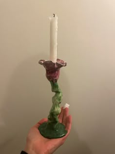 a person holding a candle in their hand with a green and purple sculpture on it