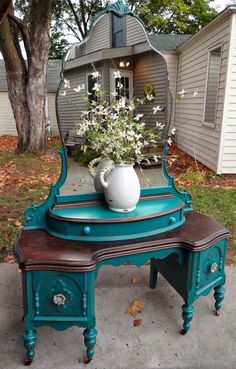 a blue vanity with a mirror on top and flowers in the vase sitting on it