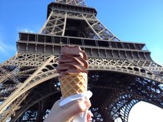 a hand holding an ice cream cone in front of the eiffel tower