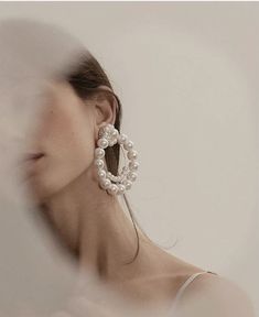 a woman wearing large earrings with pearls on them